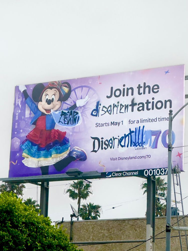 An altered Disneyland billboard in which “Disneyland” has been changed to “Disorient,” and “Join the Celebration” has been changed to “Join the disorientation.” Minnie Mouse is also featured and there’s a spray painted speech bubble coming out of her mouth that says, “READ LENIN!’