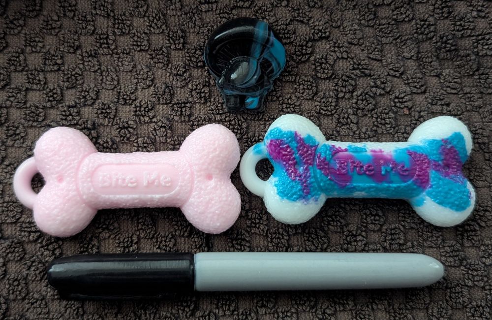 A light pink dog bone with a Jazz (design) dog bone beside it and a black marker below