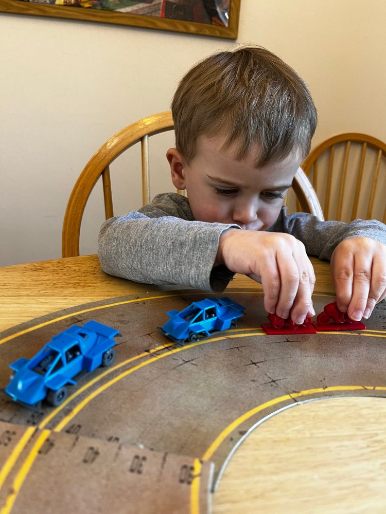 A young boy playing with unpainted model cars and motorbikes on a section of track from the game Dark Future. 