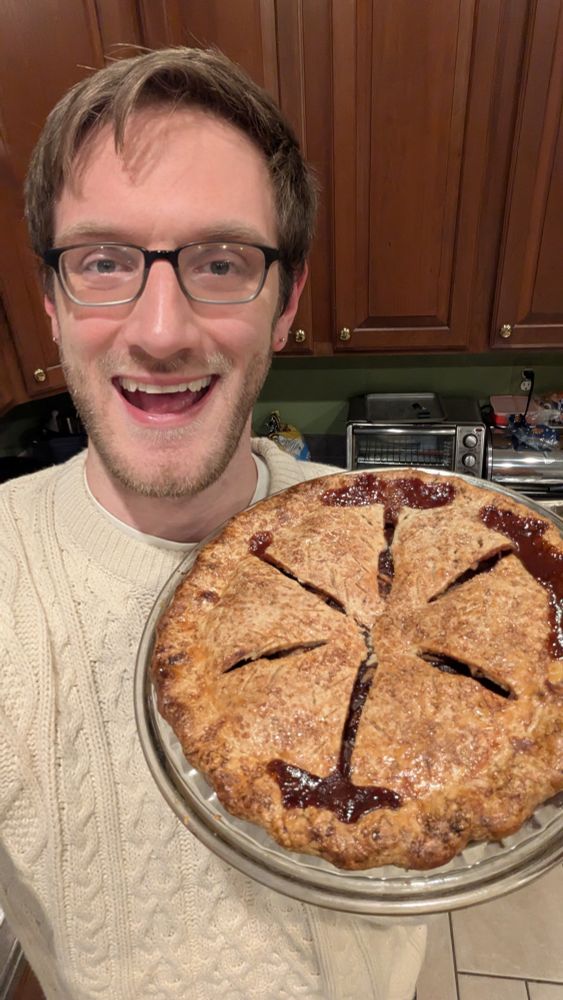 Picture of a White gay with glasses holding up a BEAUTIFUL apple and cheddar pie