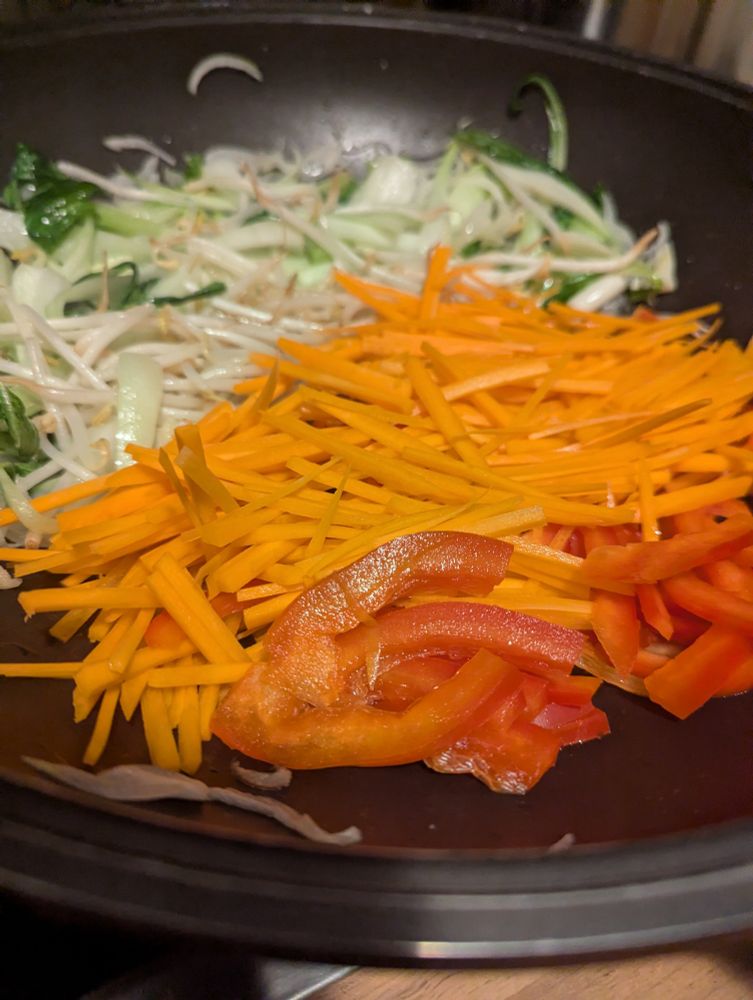 farblich sortiertes gemüse in ner Pfanne. Paprika und Karotte vorn noch relativ roh, frisch rein. Im Hintergrund heller und grüner Kram schon bisschen durcher