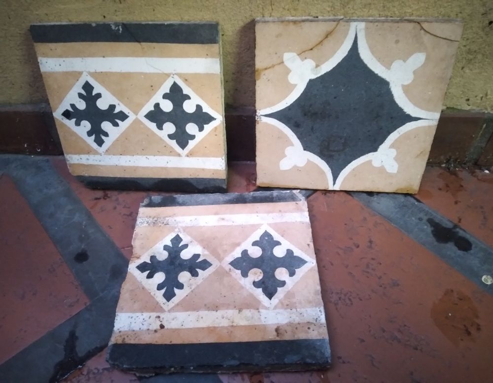 Tres baldosas hidráulicas en tonos ocre, blanco y negro, dos son de guarda y una de mosaico central