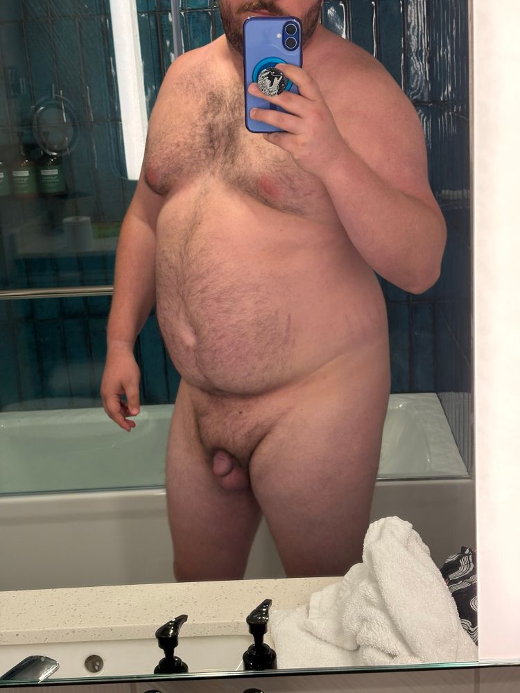 Chubby hairy man standing naked in front of a giant bathroom mirror. 