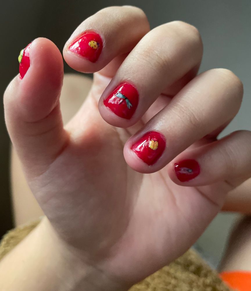 Foto da minha mão com foco nas unhas vermelhas. Elas são pequenas pq unha grande me dá agonia. Tem relevo pq é de gel e tbm tem aspecto de “molhado”. Os insetos são adesivos bem pequenos e eles tbm tem relevo do gel. Cada unha tem um inseto diferente. Tem joaninha, besouro, libélula etc