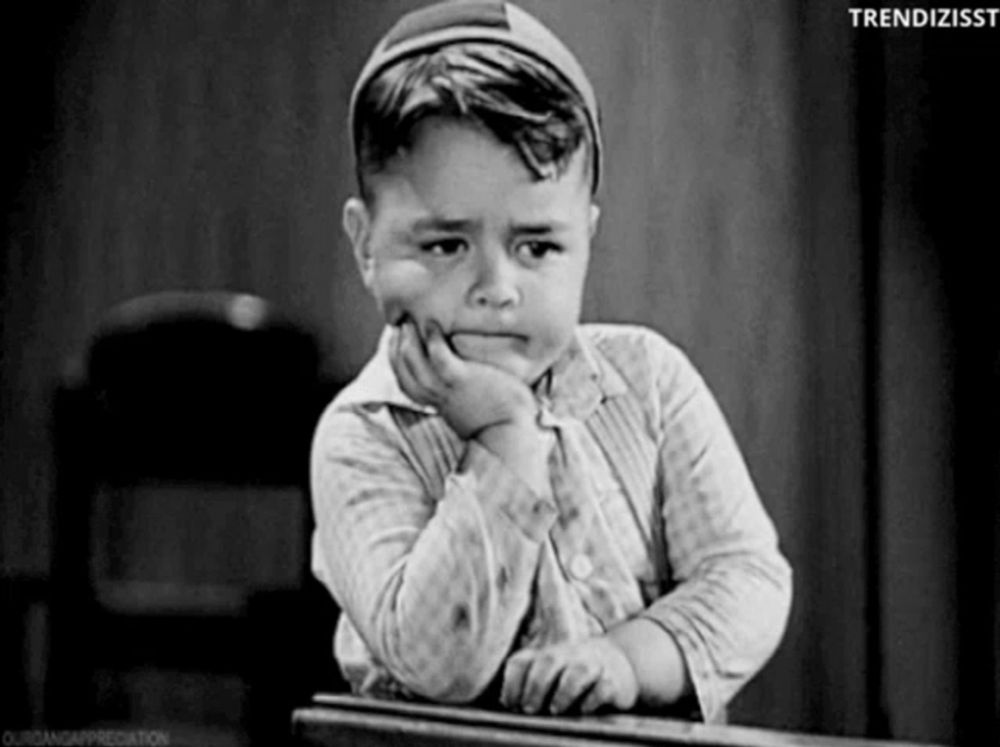 a little boy is sitting at a desk with his hand on his chin and a sad look on his face .