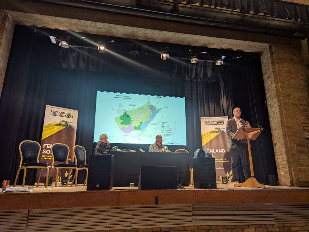 Paul Burrows, Chief Executive of the Middle Level Commissioners presenting in Ely at the Fenland SOILS conference. With map of the Middle level system behind him