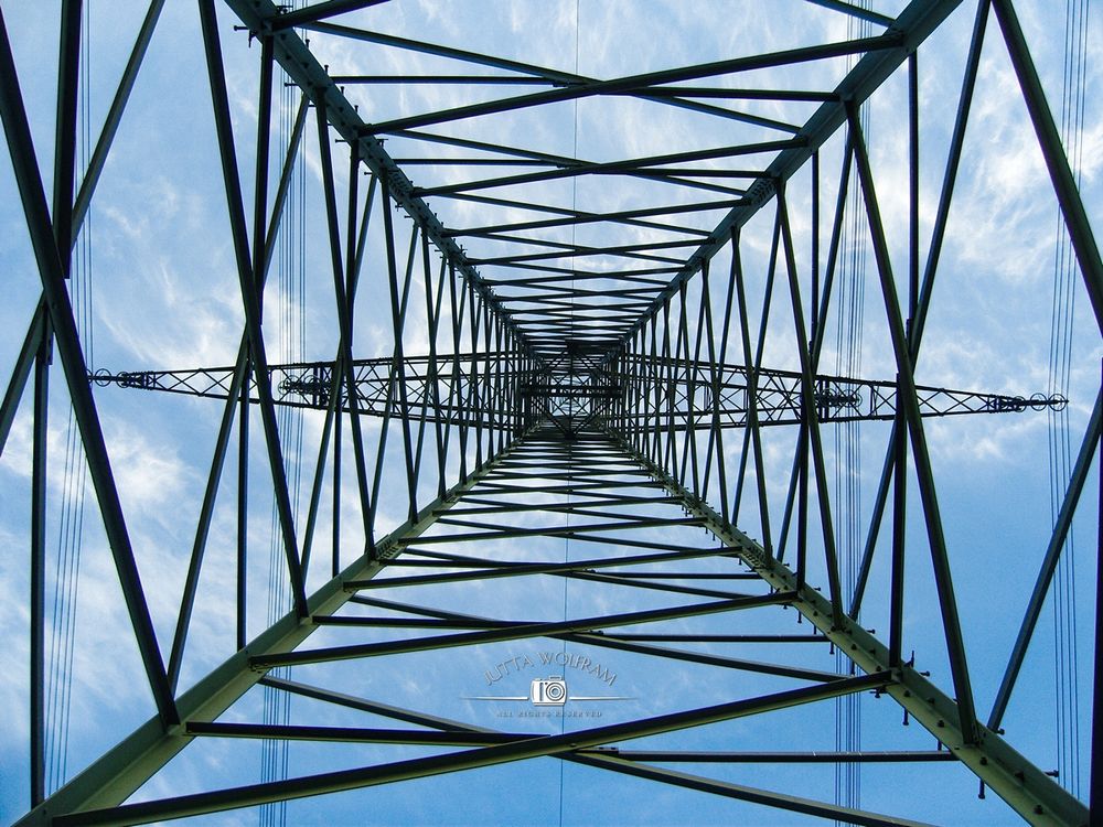 Im Bild ist hoher Strommast, der in seiner Mitte von unten aus gegen den Himmel fotografiert wurde.