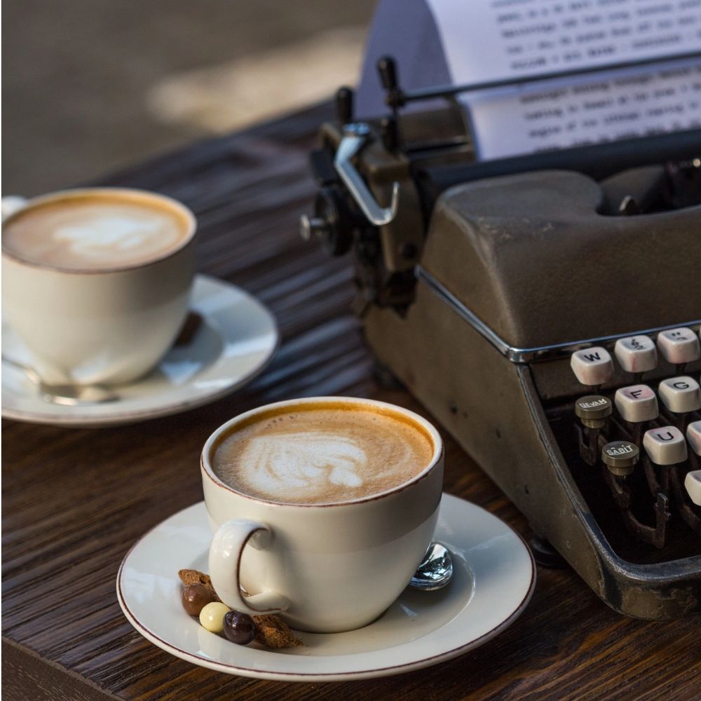 A typewriter with two cups of coffee.
