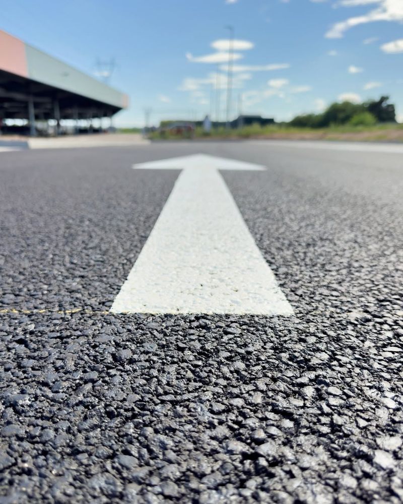 Nahaufnahme eines weißen, nach vorne gerichteten Pfeils auf Asphalt