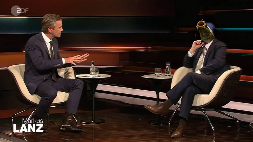 Screenshot aus einer Markus Lanz-Sendung: links gestikuliert Markus Lanz, rechts sitzt ein Anzug tragender Wels (Person mit Welskopf).