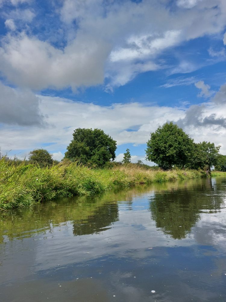 Bild von der Niers. Man sieht grüne Böschung und blauen Himmel im Hintergrund 