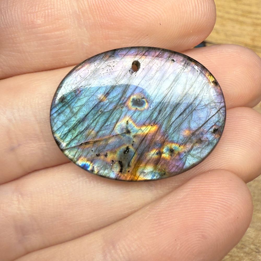 An oval cabochon of labradorite with purple, blue, yellow, and pink flash, held in a woman’s hand. 