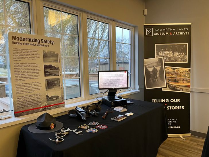 A photo of the full KLPS pop-up exhibit, featuring a panel with information and photos, and a table with various artifacts (hats, handcuffs, badges, and more) and a digital presentation.