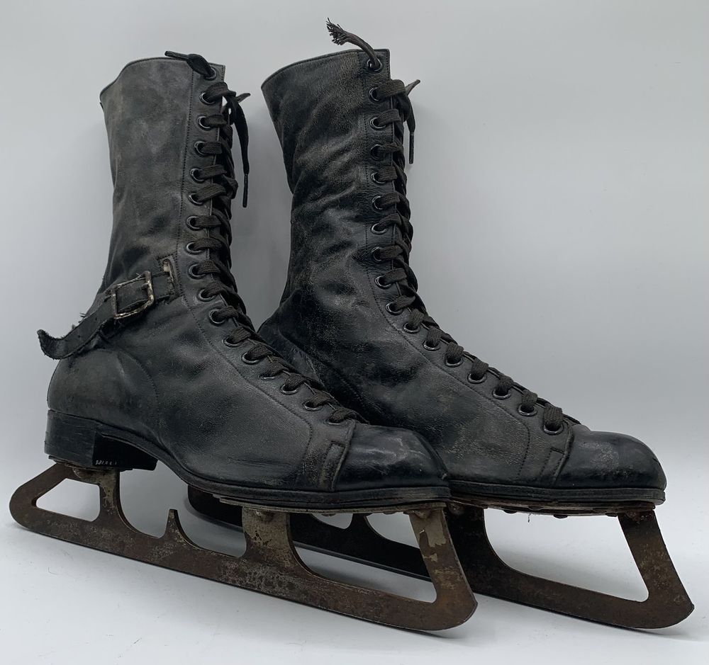 A photo of a very old pair of hockey skates, with rusty blades. 

The boot part of the skate is made of black leather. It has seventeen eyelets on each side. There is an extra strip of leather up the back. On the inside is an extra ankle support with a leather strap, which has four holes in it. The buckle is attached on the outside. Just above the buckle is a slot for the strap to go through. There is a tag with "McPhersons Lightening Hitch, patented 1903, Hockey Shoe" on it. The laces are black. The skates are size 9.5.