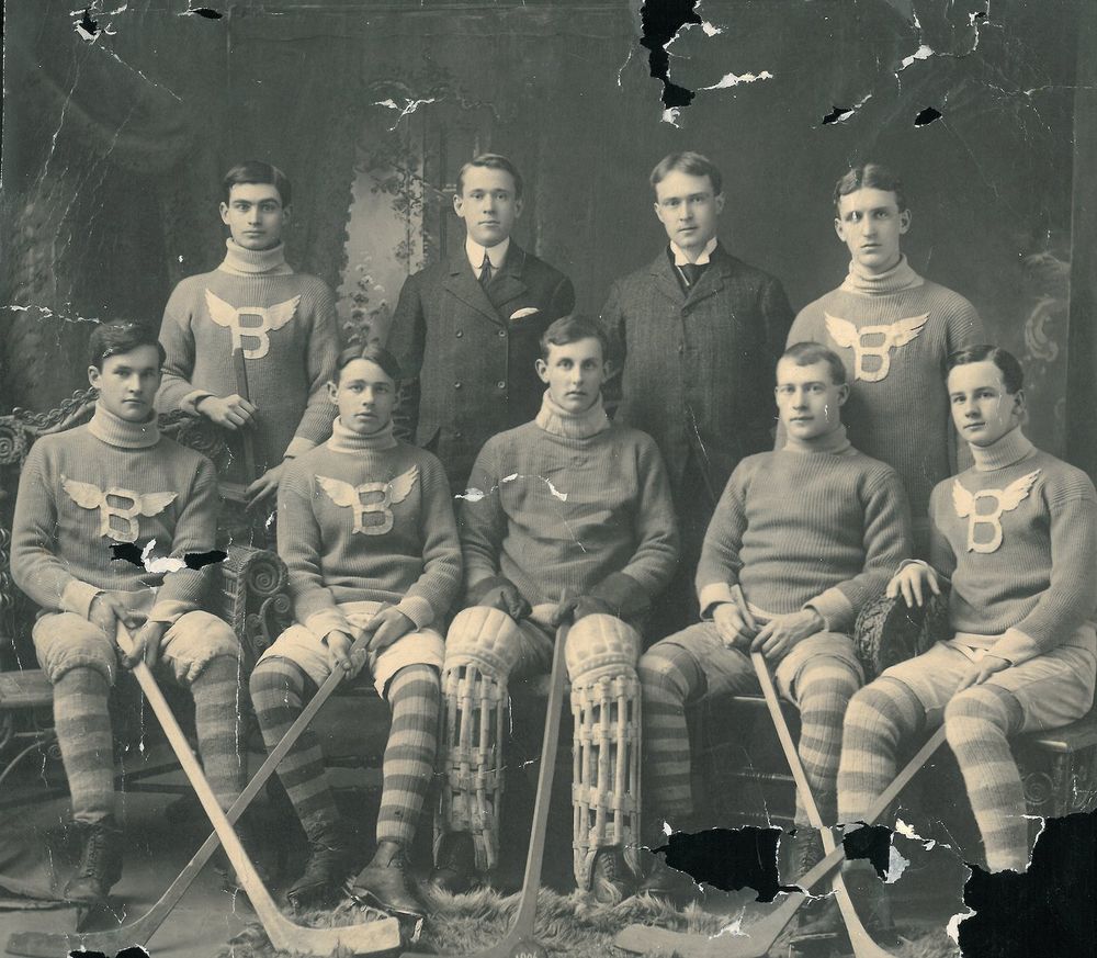 Black and White photo of 9 hockey players wearing striped leggings and sweaters emblazoned with a capital letter B with wings - Bankers Hockey Team 1906
Team members are, G.L.Warner, K.Hettger, R.L.Fortt, J.A.Macpherson, B.L.Johnston.
Top row : J.N.Tompkins, S.T.Galbraith and W.R.Geike.