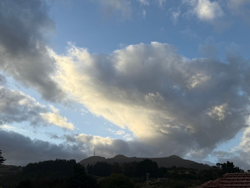 Photo of cloudy sky with a large cloud sweeping rightwards dramatically in a semi circle from top to bottom. There are hills (Kapukataumahaka) with a transmission tower across the bottom of the shot. 
