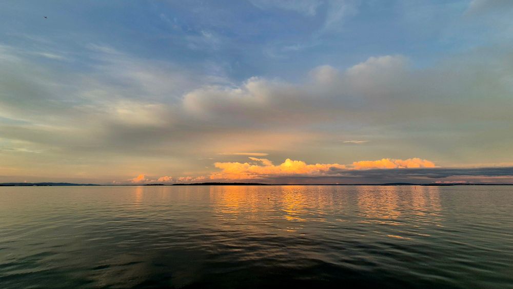 Bright pink orange and hazy clouds reflected across the fjord in a darkening blue sky