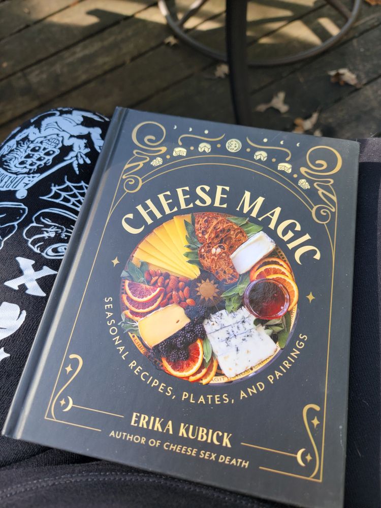 A black hardcover book with gold writing and moon decoration, titled Cheese Magic by Erika Kubick. Author or Cheese Sex Death. 