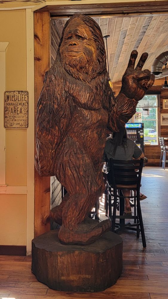 A large carved wooden bigfoot giving a peace sign gesture inside a bar.