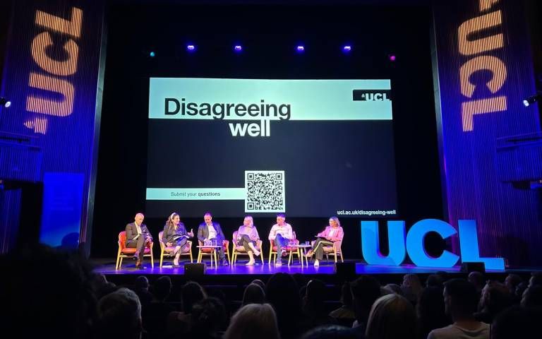 Five panellists are seated on stage at a UCL event titled "Disagreeing well," with a large screen behind them displaying a QR code for audience questions.