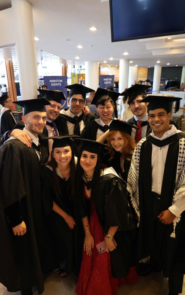 Group of graduates in caps and gowns smiling at a graduation ceremony.