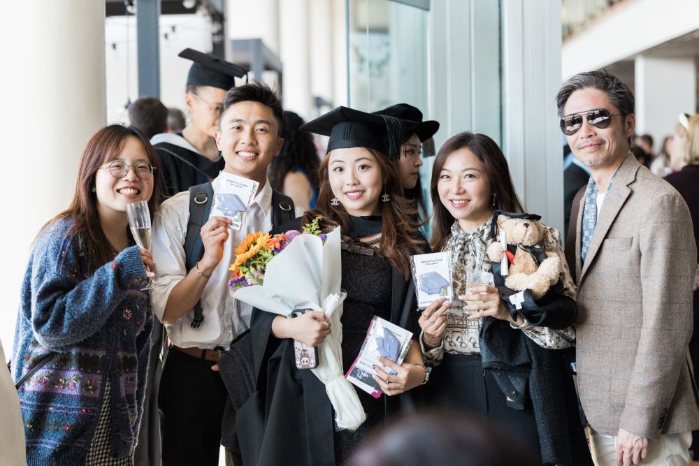 A graduate and their guests smiling at the camera, holding flowers and biscuits