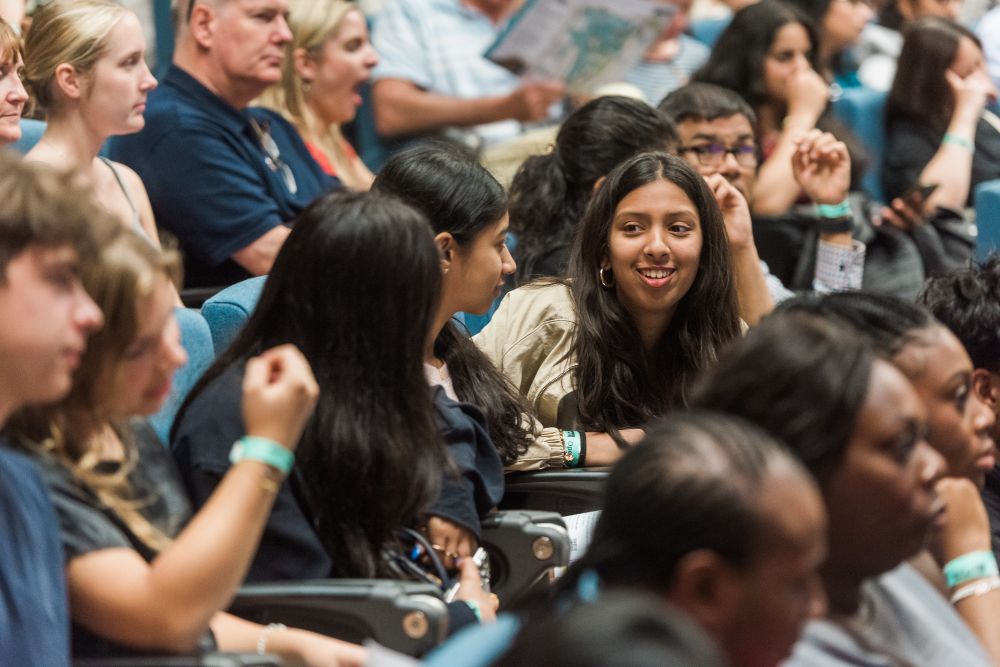 Audience members seated in a lecture hall, one person smiling at the camera.