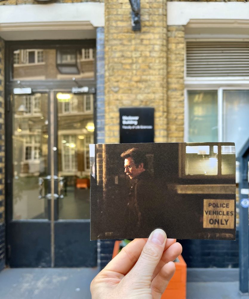 A person holds up a photograph of a scene from the movie "Batman Begins",  aligning it with the actual filming location visible in the background.