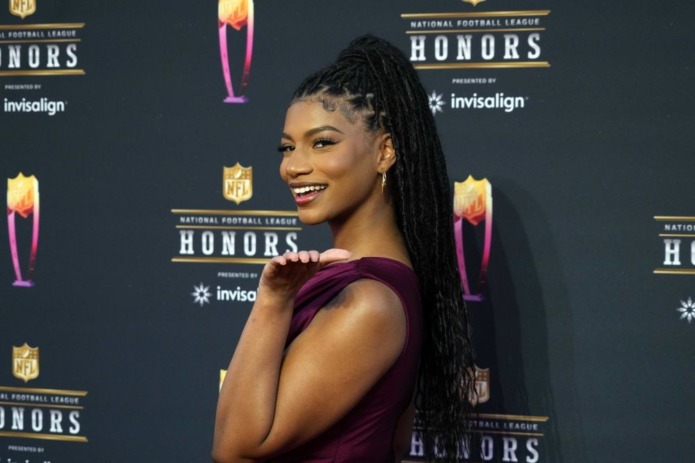 Taylor Rooks turned sideways with a plum colored dress, in front of an "NFL Honors" step-and-repeat