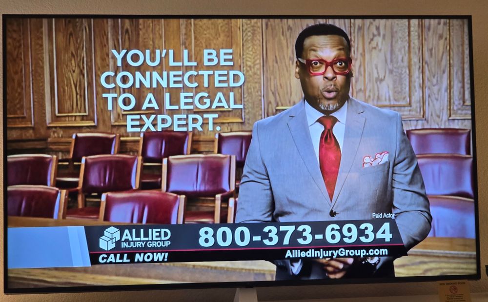 Photo of a lawyer tv commercial, featuring a man in a grey suit, and red glasses and tie.