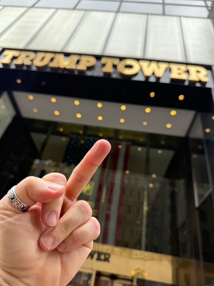 The photographer is flipping off Trump Tower (background) with their left hand (foreground)