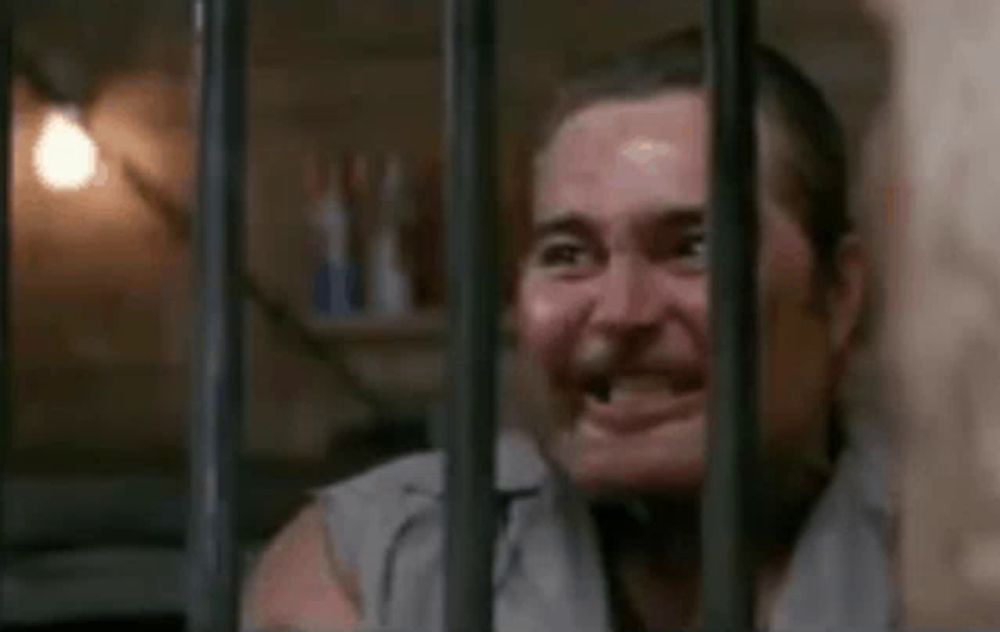 a man is behind bars in a jail cell and making a face .