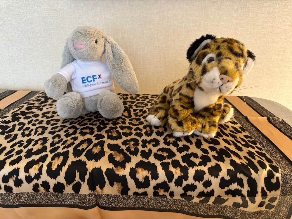 a stuffed bunny in a white ECFx:  Intelligent Automation shirt and a stuffed leopard, both on top of a leopard print bandana