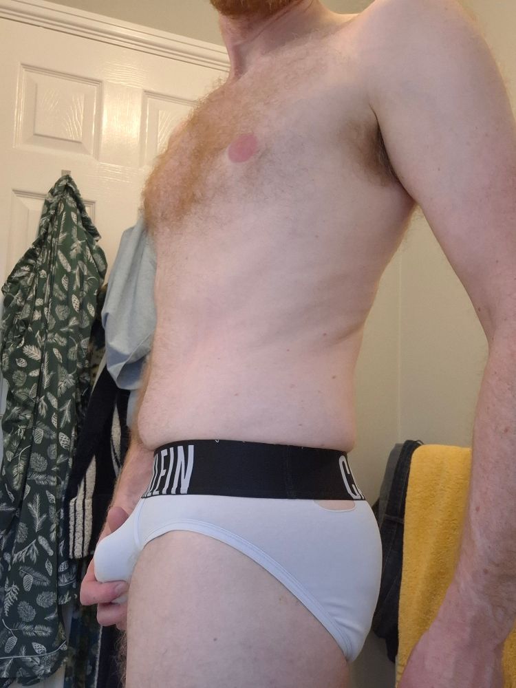 Man standing in his white breifs which have a small tear on the seam along the waistband. 