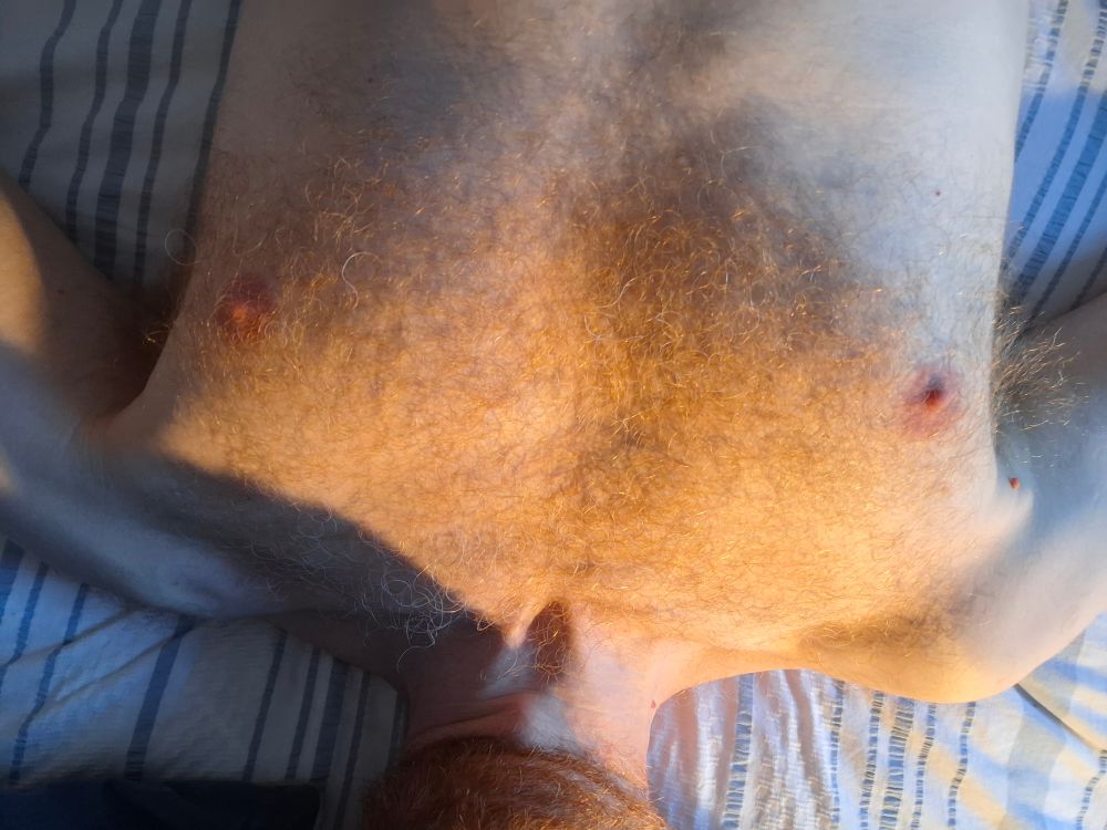 Man laying on a bed. His ginger chest hair gleaming in the light. 