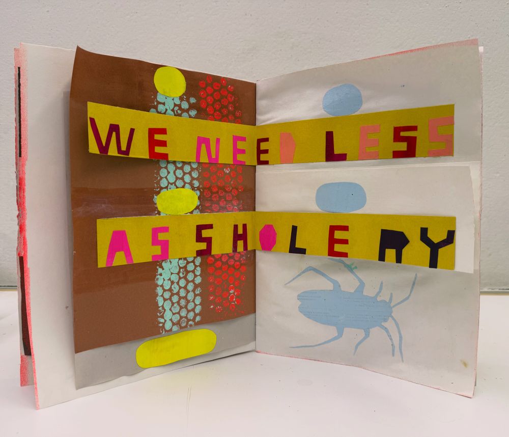 A photo of a hand made sketchbook spread standing up on edge. The left side is a brown sheet of construction paper with a texture in light blue and orange made by painting on bubble wrap. On the left side it’s a white page with light blue circles and a silhouette of a cockroach. Over the spread are two strip of yellow paper. The top strip has “we need less” written out using cut paper. Two inches down is another strip of yellow paper with “assholery” written using cut paper. Art by Martha Rich.  