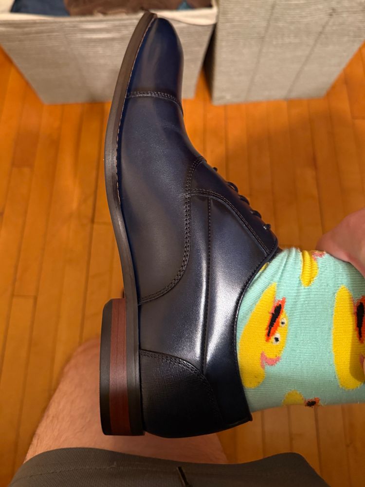 A pic of a foot wearing a navy blue dress shoe and mint & yellow duckie socks.