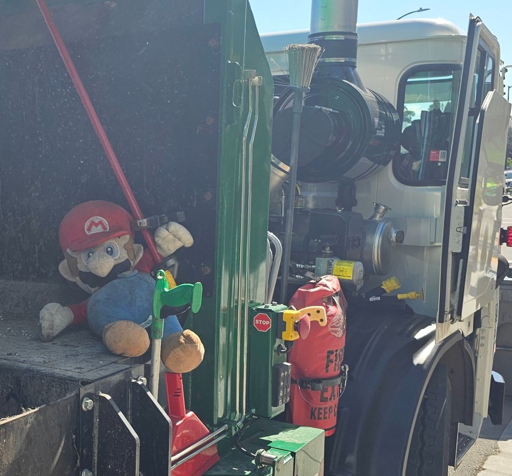 A stuffed mario plush on the back of a garbage truck