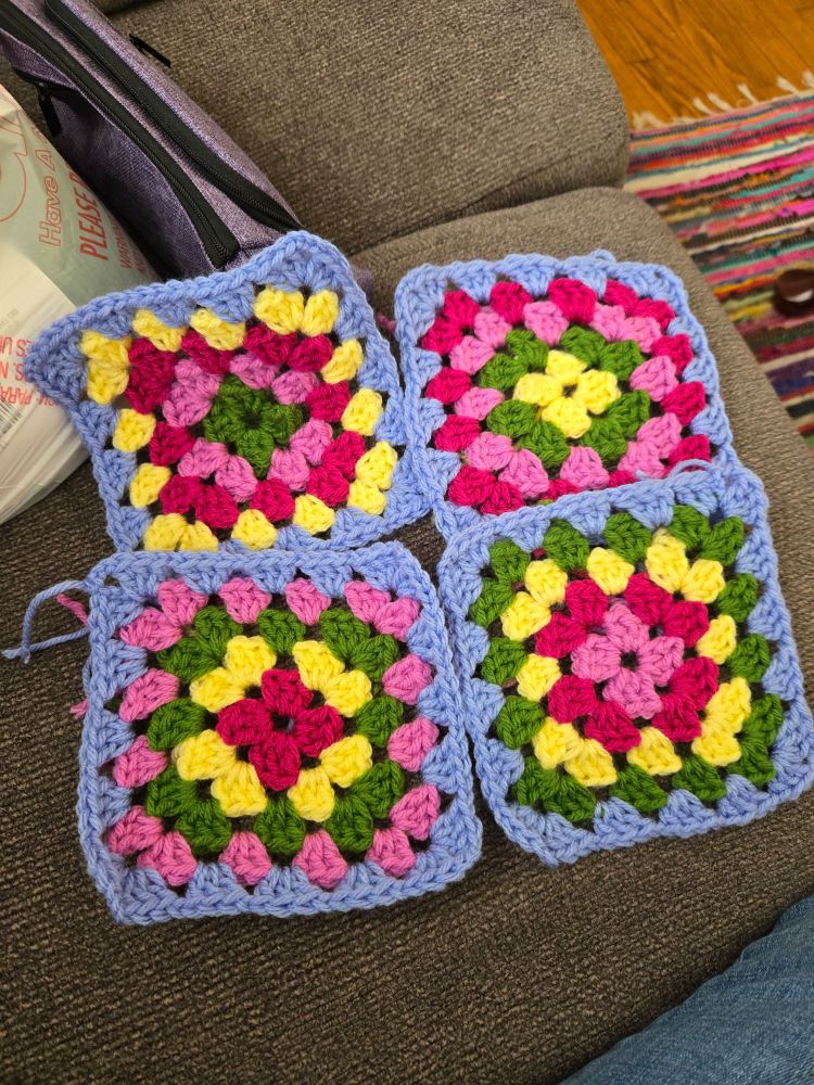 Four separate crocheted granny squares in yellow, green, and two shades of pink, with a periwinkle background. 