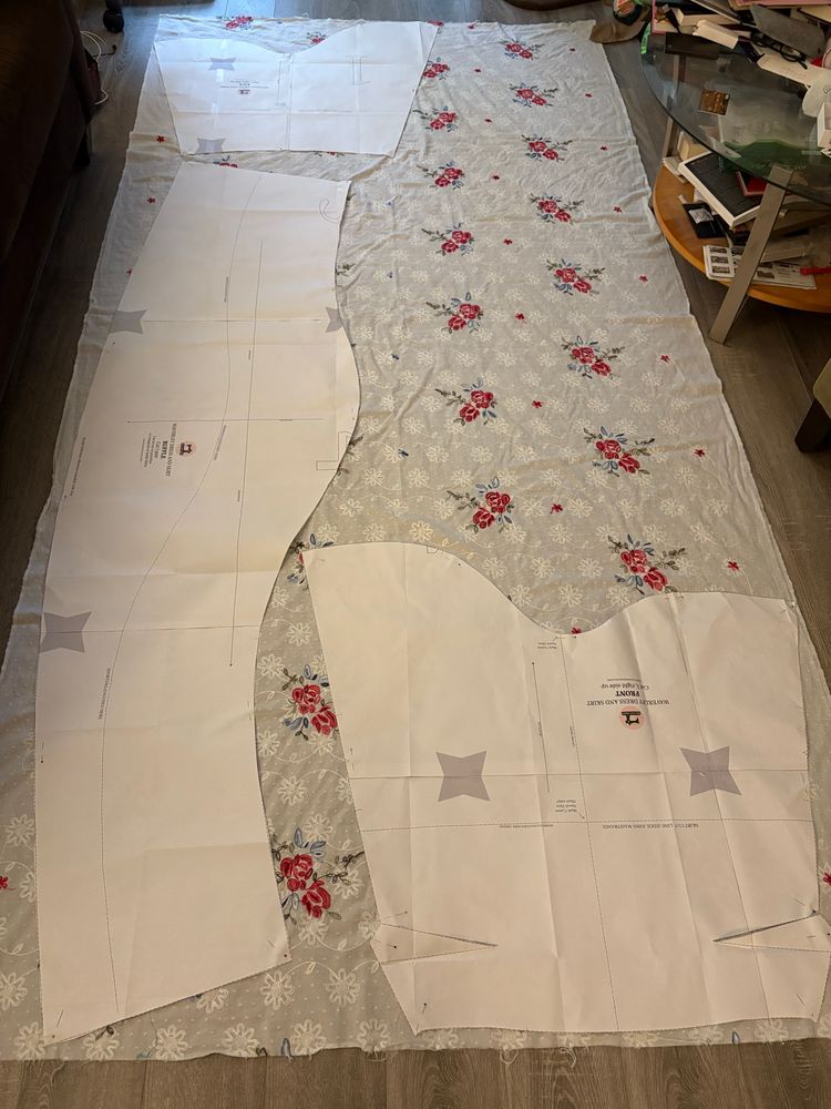 A length of white fabric with embroidered flowers laid out on the floor with sewing pattern pieces sitting on top