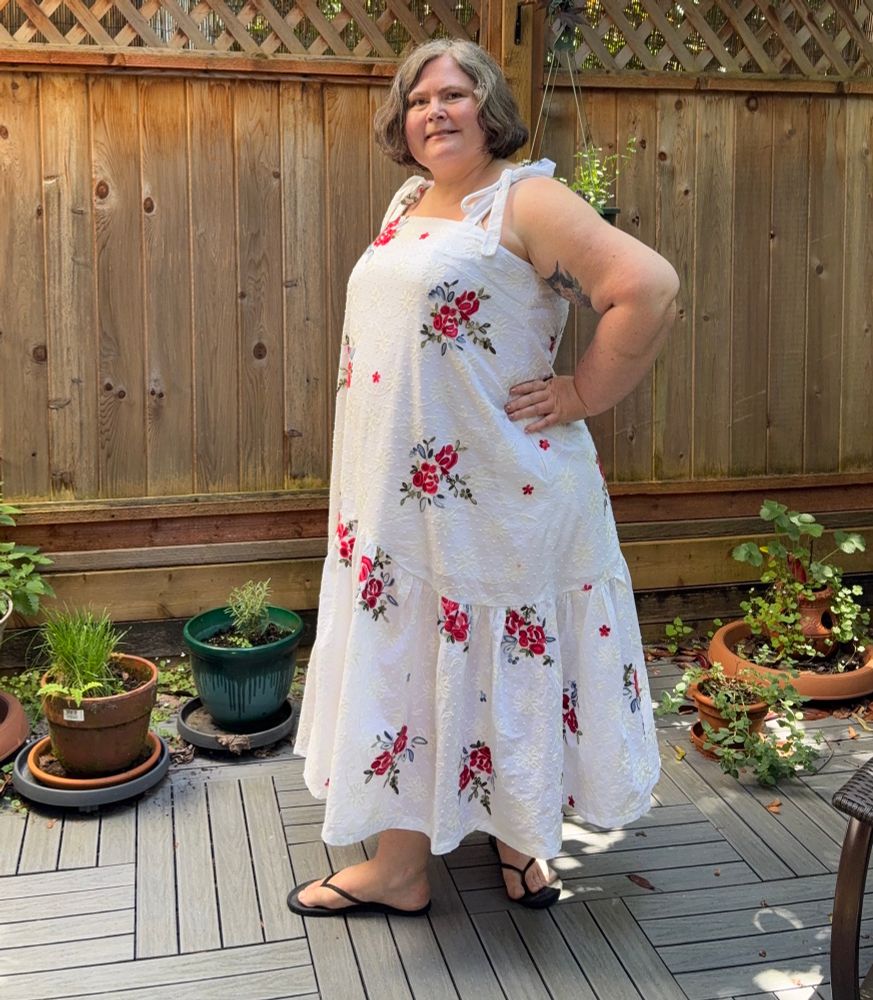 A 3/4 view of a woman in a white sundress with red flowers 