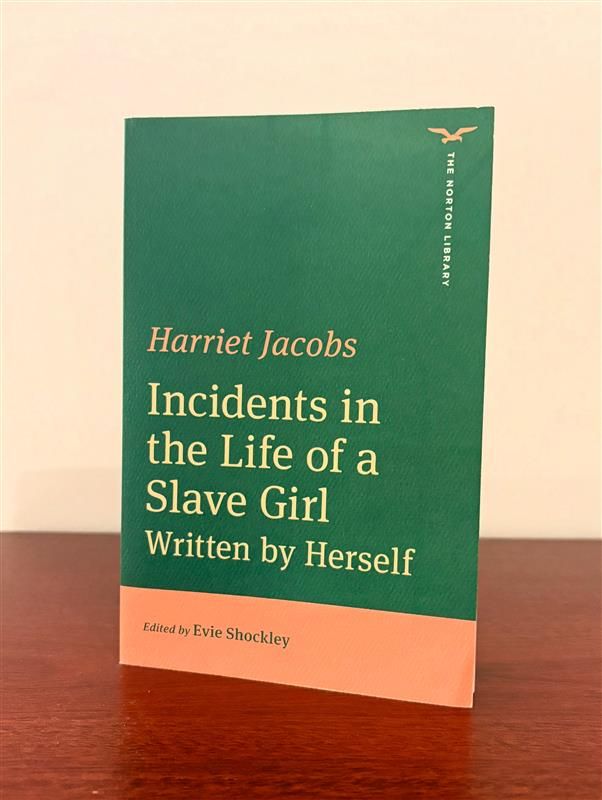 Green and orange color blocked cover of Harriet Jacobs's Incidents in the Life of a Slave Girl (The Norton Library) edited by Evie Shockley on a wooden table with a white background. 
