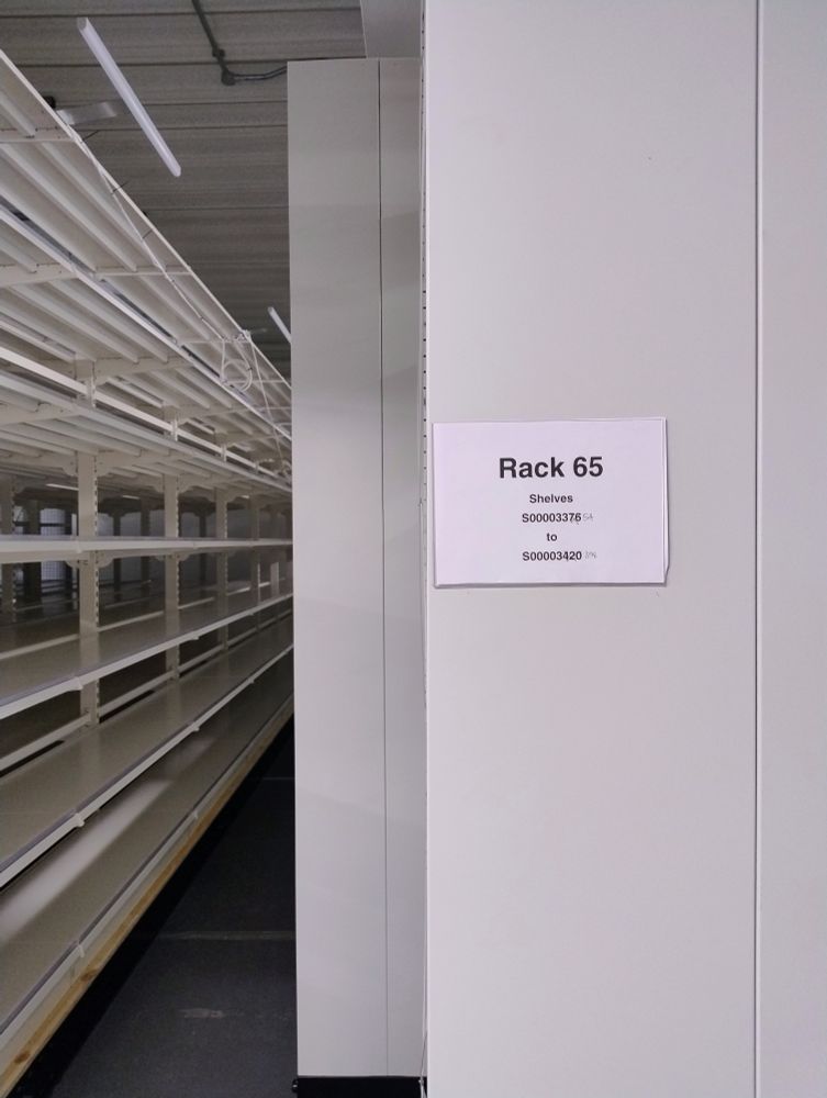Rack label on the end of a static rack at Oldham Archives, with roller racking for plan storage on the left.