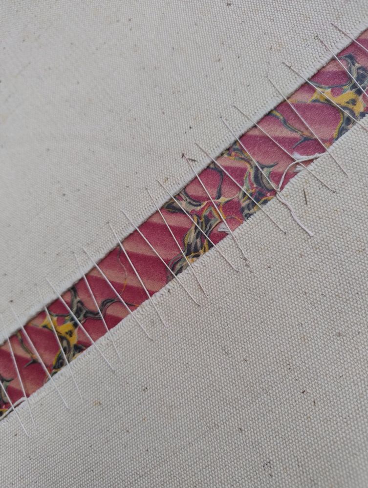 Tacked lacing stitch inside an archive volume that has been covered with a canvas book jacket. The stitches have been photographed diagonally . Marbled paper can be seen behind the stitches.