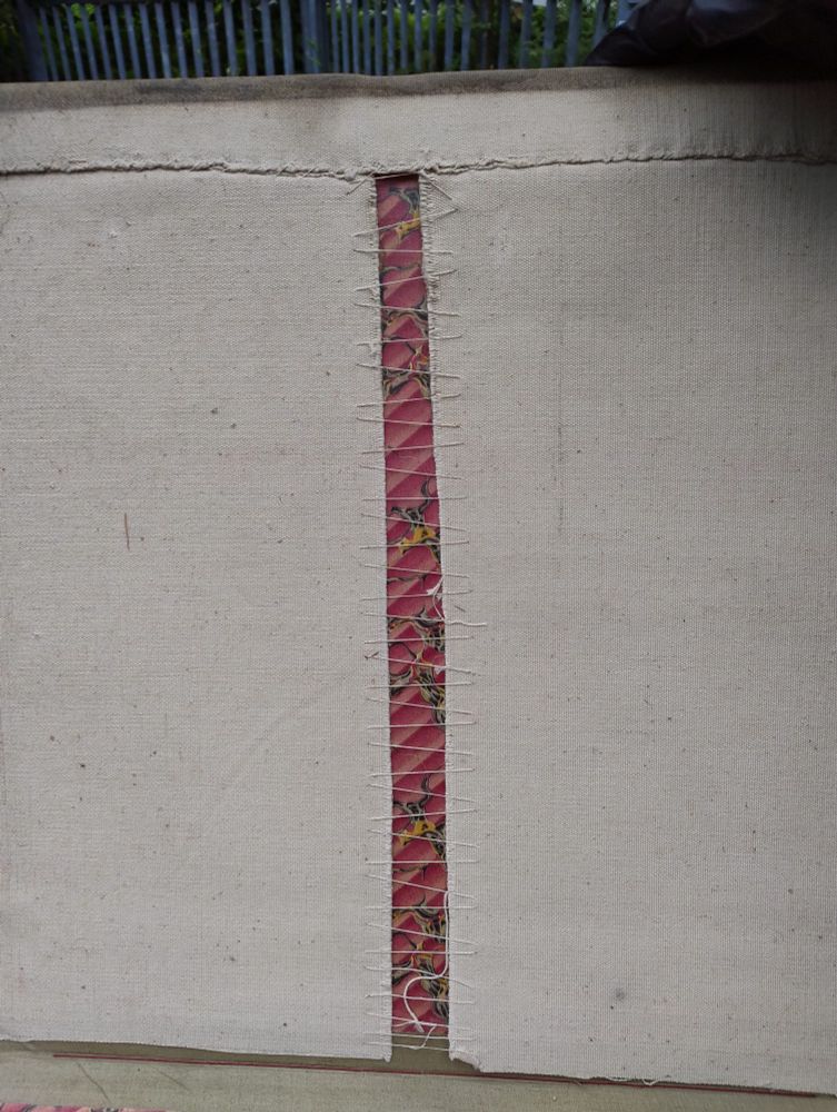 Tacked lacing stitch inside an archive volume that has been covered with a canvas book jacket. The stitches run top to bottom. Marbled paper can be seen behind the stitches.