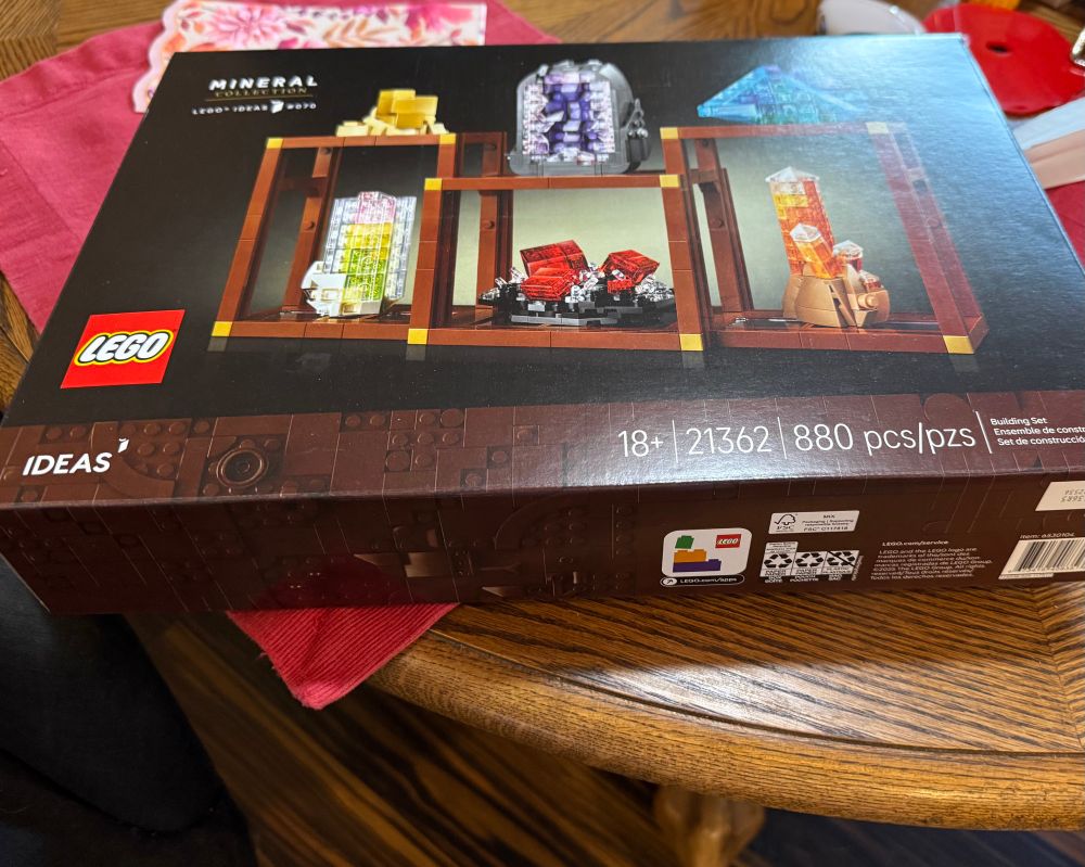 Lego ideas mineral set, still in box, on a wood table and a red place mat, with a fall-colored napkin in the background 