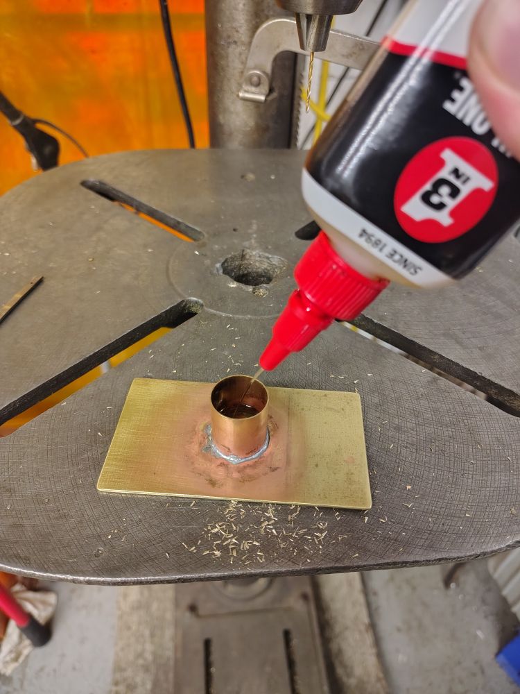 a brass tube crudely soldered orthogonally to a brass plate, creating a sort of pot with a wide flat base. seen here being filled with 3 in 1 oil for use with a drill press