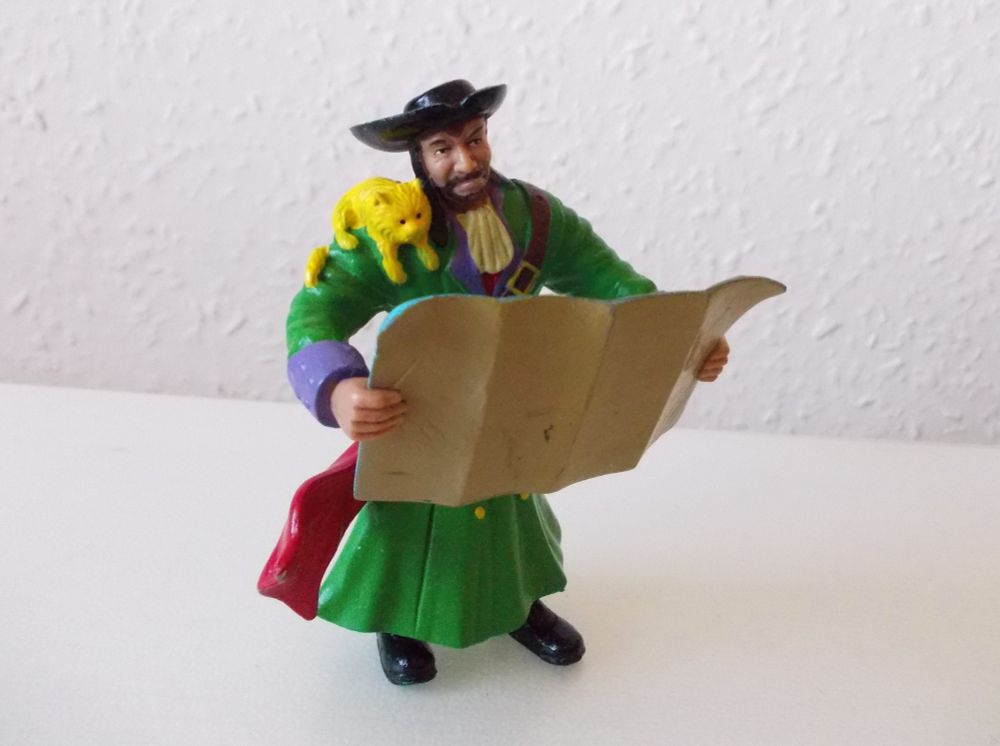 Picture shows a small toy plastic figurine of a pirate looking at a treasure map. On the pirate's shoulder sits a small cat, also looking at the map.