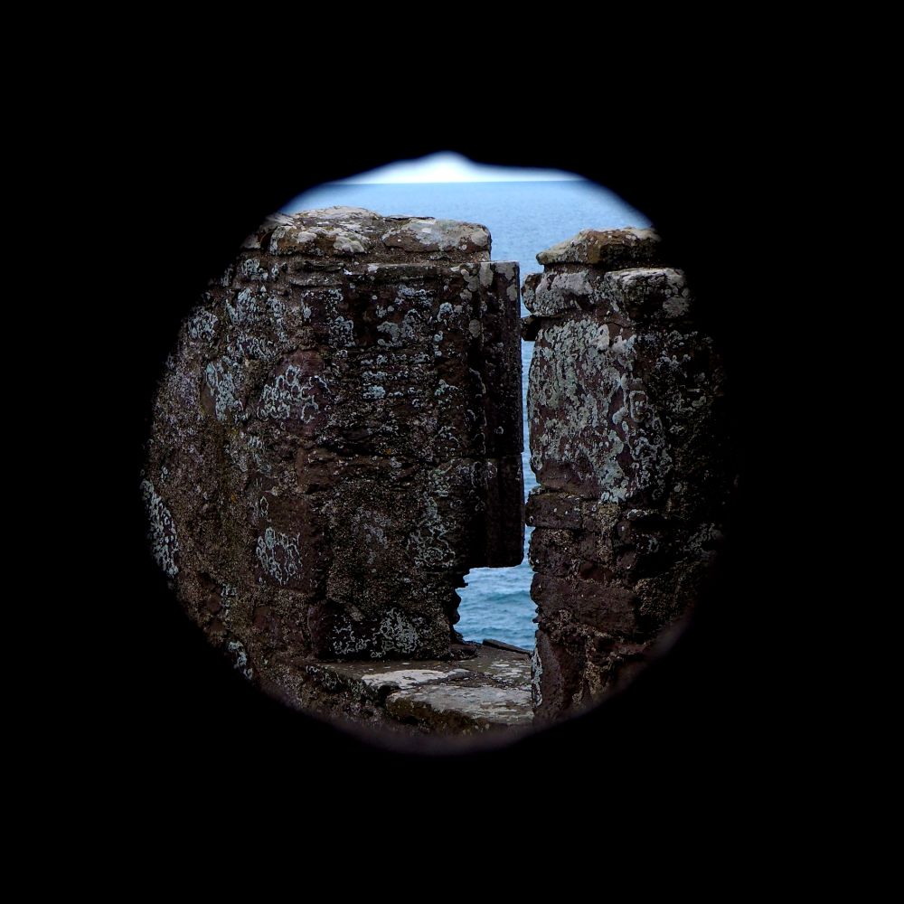 View through a circular gunloop, looking onto battlements with a glimpse of sea beyond.