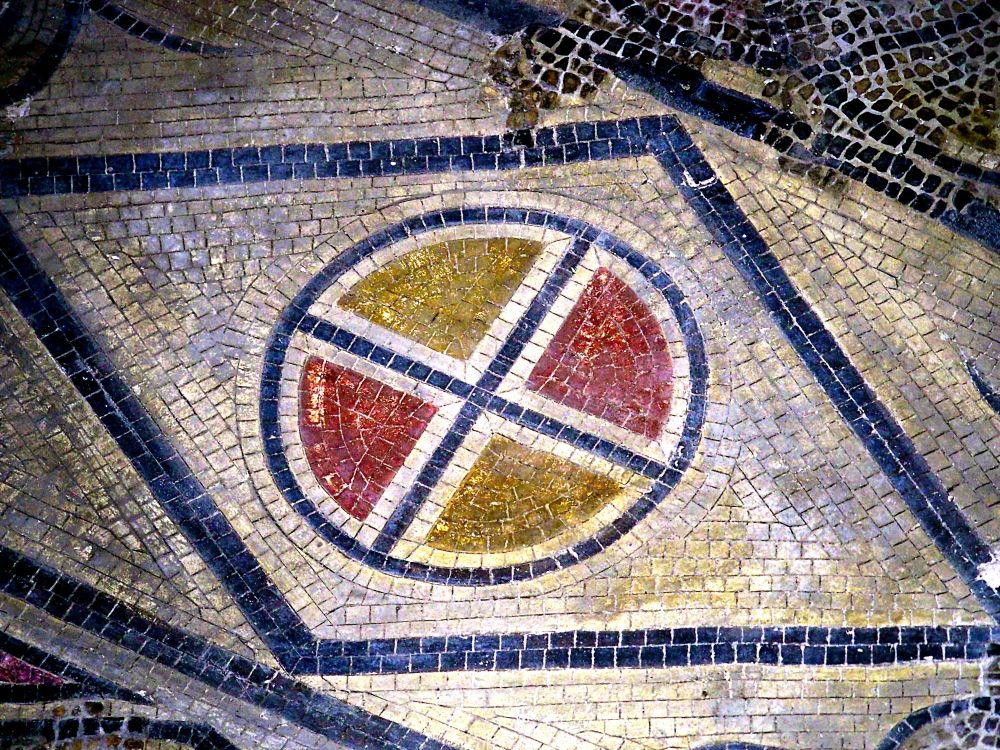 Mosaic flooring displaying a geometric pattern. A circle picked out in black, quartered in red and yellow, sits on a white background within black lines forming a lozenge shape.